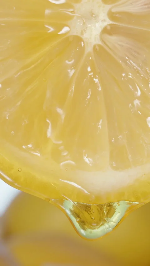 A slice of Lemon drips honey from it, behind sliced lemons against the sky. Vert Stock Footage 234135185
