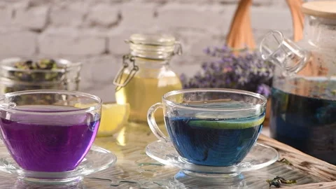 A slice of lemon is dropped into a cup of Butterfly Pea Tea Stock Footage 337571623