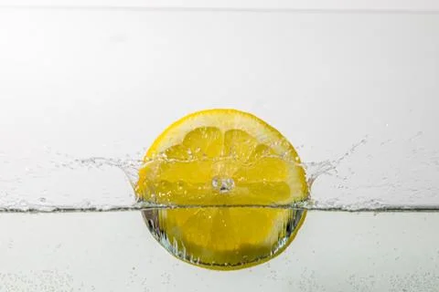 Slice of lemon falls into the water from above and creates water splashes Stock Photos