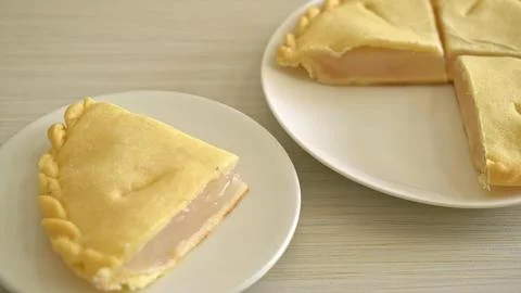 Slice of lemon pie on a white plate with a full pie in the background Stock Photos