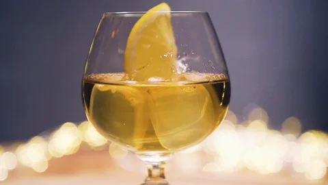 Slice of lemon,lime dropped into glass full of Whisky, Whiskey Stock Footage 128922624
