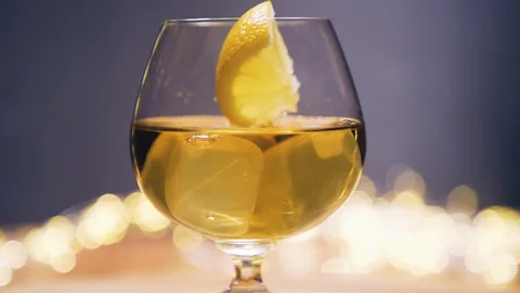 Slice of lemon,lime dropped into glass full of Whisky, Whiskey Stock Footage 128922672