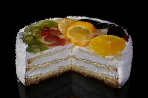 A slice of a luxurious cake with fruit oranges kiwi gooseberry sprinkled with Stock Photos