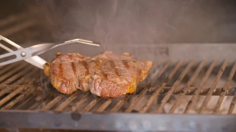 Slice of meat being flipped over a bbq grill with tongs Stock Footage 85812307
