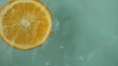 Slice of orange drops into water causing playful splashes As orange slice hits Stock Footage 269995238