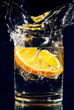 Slice of orange falling down in glass with water on deep blue Foto stock