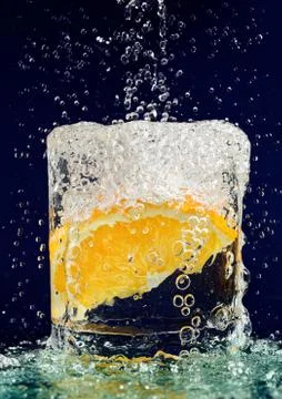 Slice of orange falling down in glass with water on deep blue Foto stock