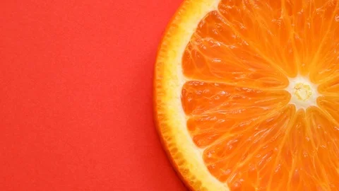 Slice of orange rotating close-up on red background Stock Footage 106062550