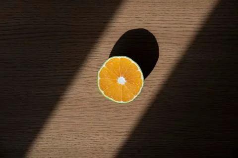 A slice of orange is standing on the top of the table with sunlight and contrast Stock Photos