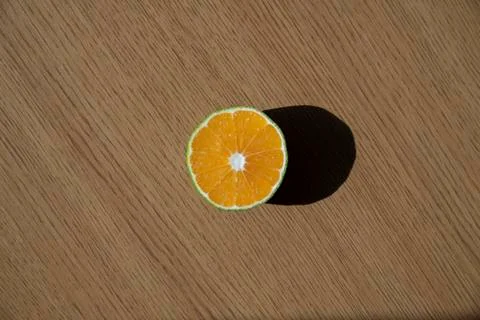 A slice of orange is standing on the top of the table with sunlight and contrast Stock Photos