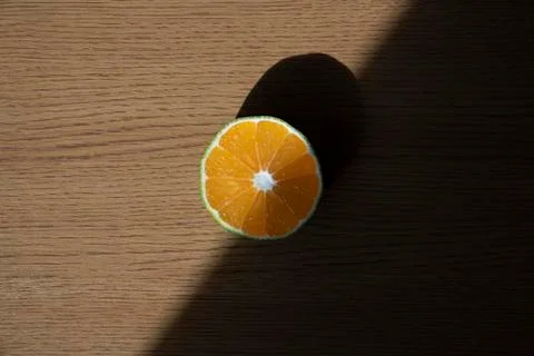 A slice of orange is standing on the top of the table with sunlight and contrast Stock Photos