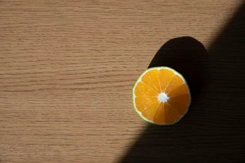 A slice of orange is standing on the top of the table with sunlight and contrast Stock Photos