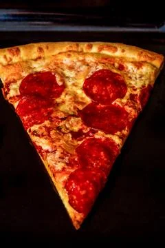 A slice of pizza on a black baking sheet in the oven. Stock Photos