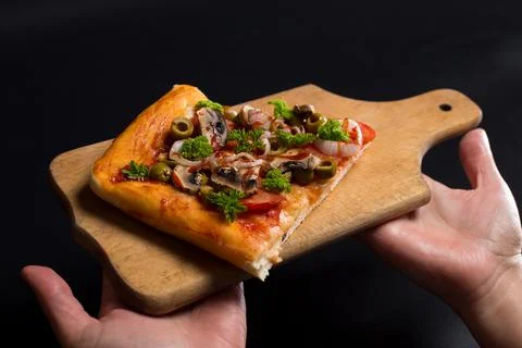 Slice of pizza on kitchen board. Serving pizza on black. Stock Photos