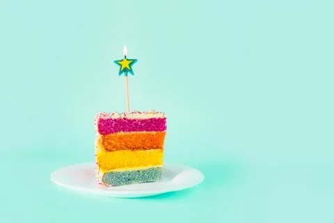 Slice of Rainbow cake with birning candle in the shape of star on white round Stock Photos
