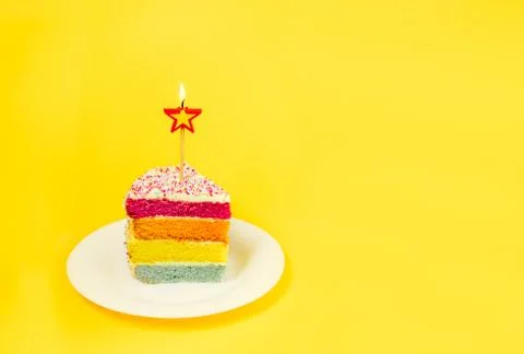 Slice of Rainbow cake with birning candle in the shape of star on white round Foto stock