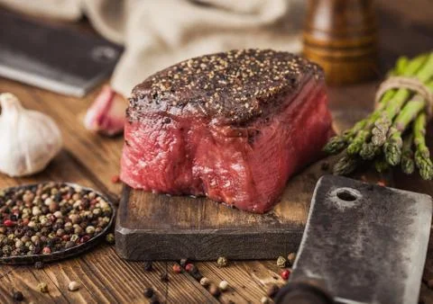 Slice of Raw Beef Topside Joint with Salt and Pepper on wooden chopping board Stock Photos