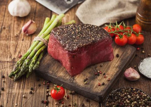 Slice of Raw Beef Topside Joint with Salt and Pepper on wooden chopping board Stock Photos