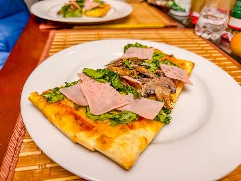 Slice of rectangular pizza with ham, mushrooms, and fresh lettuce on white .. Stock Photos
