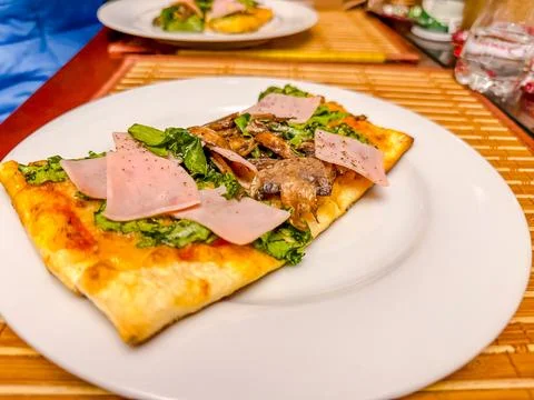 Slice of rectangular pizza with ham, mushrooms, and fresh lettuce on white .. Stock Photos