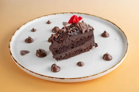 A slice of rich chocolate layer cake topped with a red flower, Stock Photos