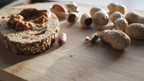 Slice of seeded bread with peanut butter and peanuts on a wooden board Stock Footage 298195655