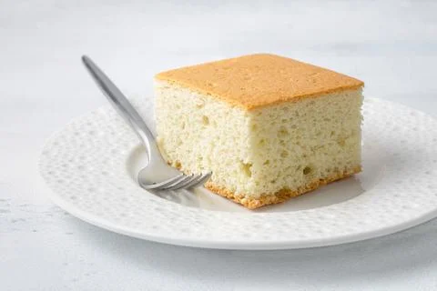 Slice of sponge cake on white ceramic plate with fork, close-up, minimal de.. Photos