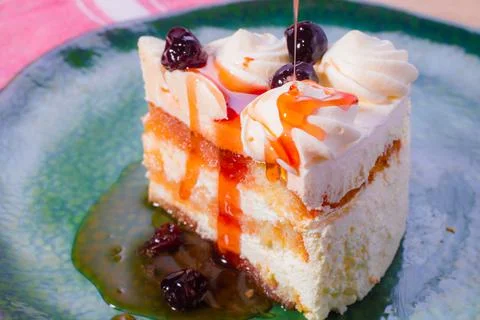Slice of sponge cake with white cream and red cherry syrup. Stock Photos