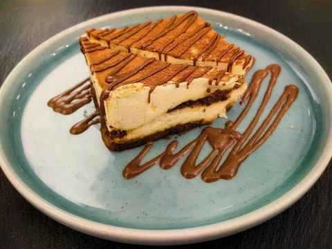 A slice of tiramisu with a sprinkle of coco powder and chocolate sauce on top. Foto stock