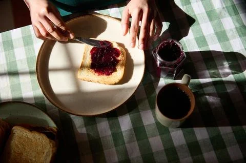A slice of toast spread with dark jam rests on a plate as a jam jar and coffe Foto stock