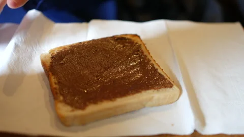 A slice of white bread being spread with chocolate hazelnut spread using a Stock Footage 318786858