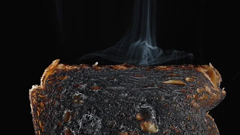 A slice of white bread is burnt, smoke is coming from it. Slow motion on a black 스톡 동영상 233521454