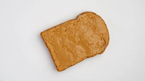 Slice whole-wheat bread covered with peanut butter on White rotating. 库存影片 250302336
