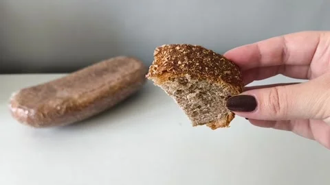 A slice of whole wheat yeast bread in his hand, a loaf of dark flour sourdough 库存影片 330040132
