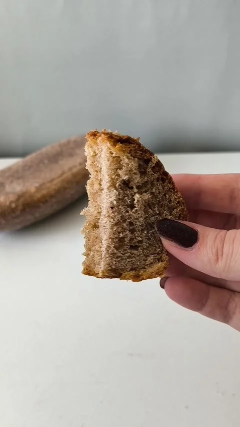 A slice of whole wheat yeast bread in his hand, a loaf of dark flour sourdough 库存影片 330040137