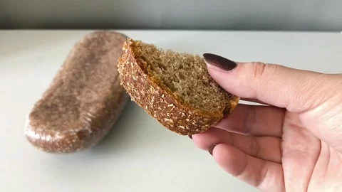 A slice of whole wheat yeast bread in his hand, a loaf of dark flour sourdough 库存影片 330040142