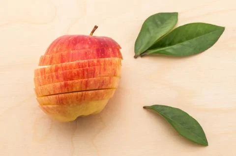 The sliced apple that retained its shape rests on a wooden table with green f Stock Photos