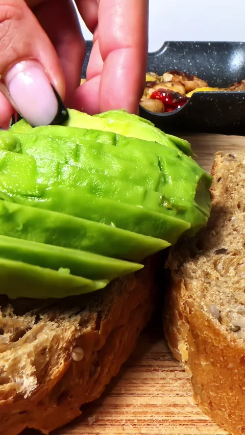 Sliced Avocado Being Placed on Whole Grain Bread Stock Footage 337929581