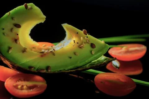 Sliced avocado, halfs of cherry tomatoes and chives on the black reflective Stock Photos