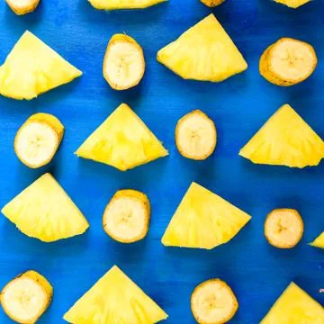 Sliced banana, pineapple pattern on blue background, wooden table. Stock Photos