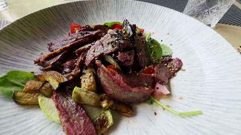 Sliced beef and roasted vegetable salad with fresh greens, tomatoes, and sesame Stock Footage 341658043