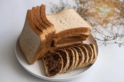 The sliced bread put in white dish,on white desk,blurry light around. 库存照片