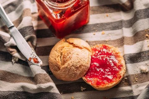 Sliced bread with strawberry jam, jam jar and a dirty knife on a tablecloth Stock Photos