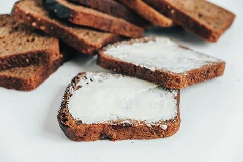 Sliced of brown bread with butter on a white wooden background. Top view. C.. Stock Photos