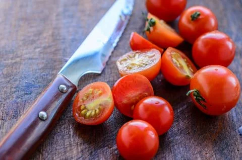 Sliced cherry tomatoes and a sharp knife with a wooden handle Stock Photos