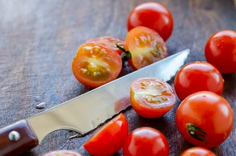 Sliced cherry tomatoes and a sharp knife with a wooden handle Stock Photos
