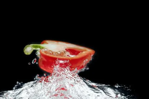 Sliced colored bell peppers splashed on black background Stock Photos
