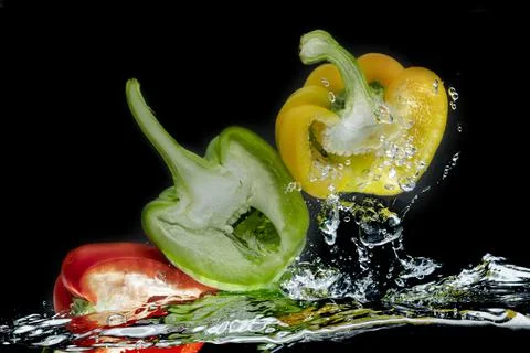 Sliced colored bell peppers splashed on black background Stock Photos
