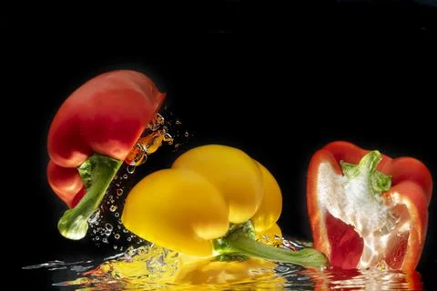 Sliced colored bell peppers splashed on black background Stock Photos