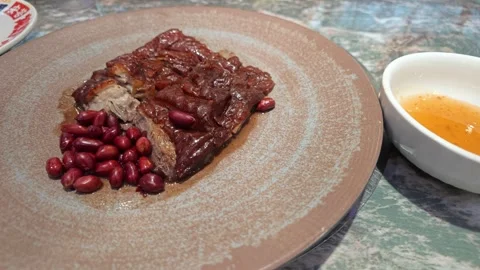 Sliced Crispy Glazed Roasted Meat with Red Peanuts on Textured Ceramic Plate 스톡 동영상 339330580